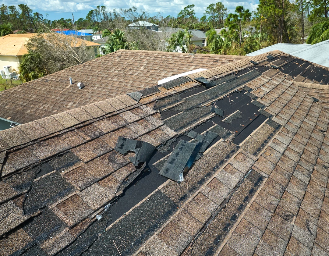 Damaged asphalt shingle roof with missing and torn shingles needing repair after storm damage, which could be covered under a home warranty plan