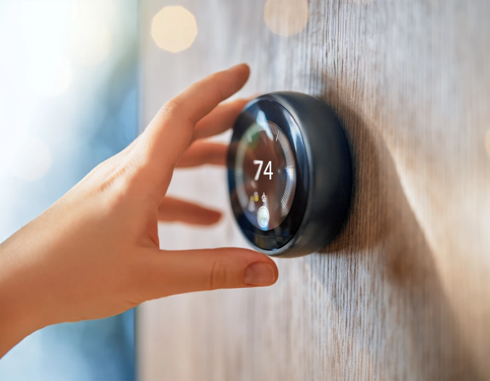 A woman's hand setting the temperature on her wall mounted smart home thermostat.