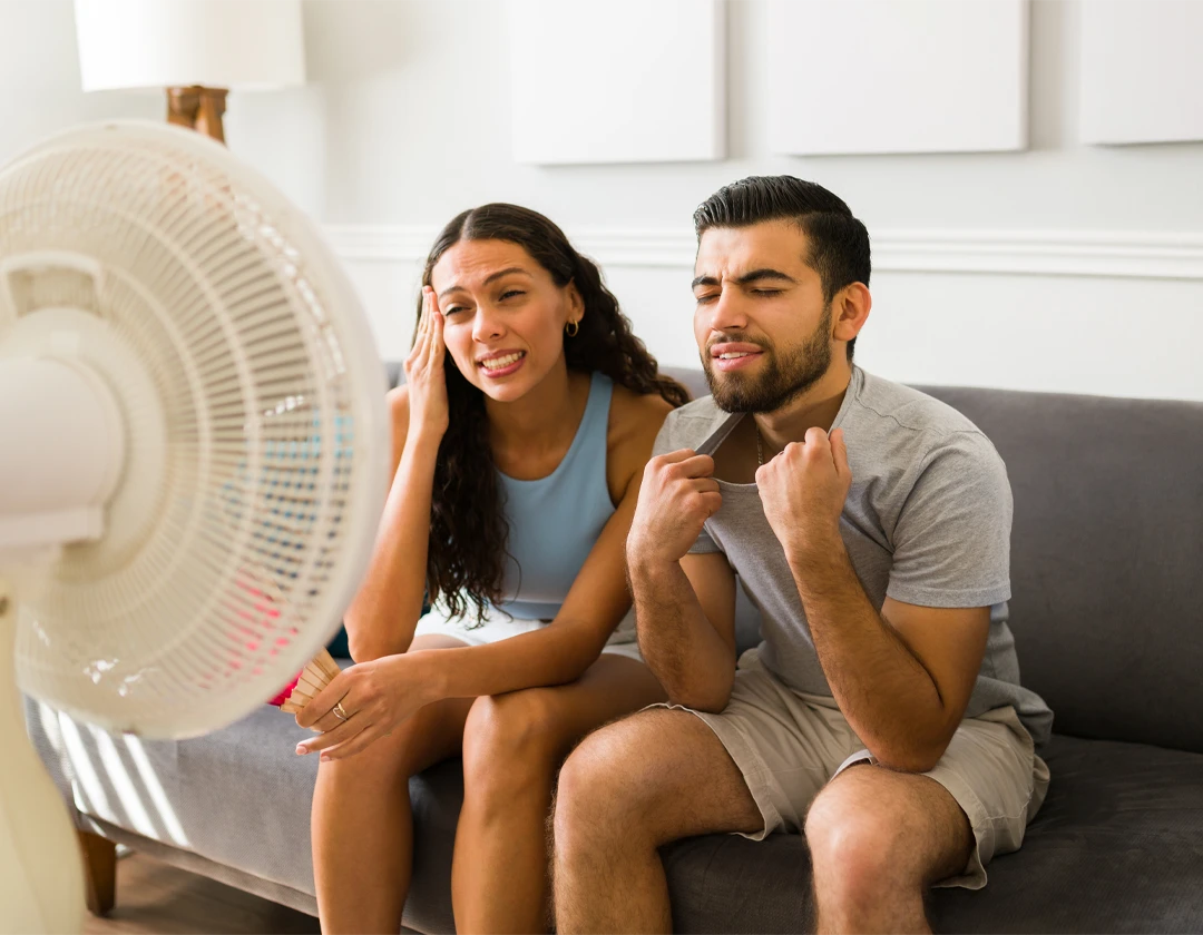 Homeowners struggling with indoor heat and relying on a fan while waiting for air conditioning repair.
