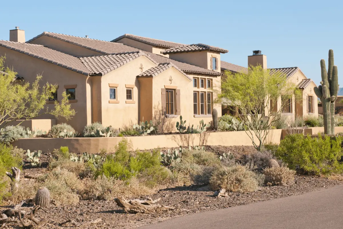 Arizona-style brown home surrounded by desert cacti beneath a bright blue sky