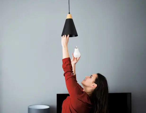 A woman using her DIY skills to change a bulb in one of her home's light fixtures.