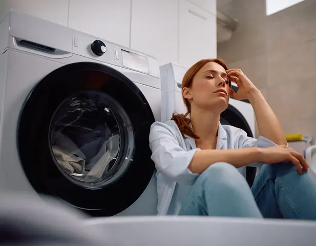 A woman sitting beside her washing machine that has broken down, due to lack of basic maintenance.