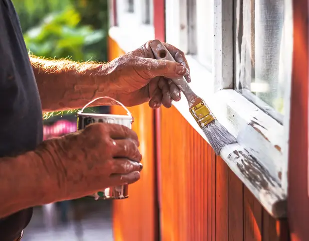 A homeowner making autumn home improvements by painting the outdoor windowsills.