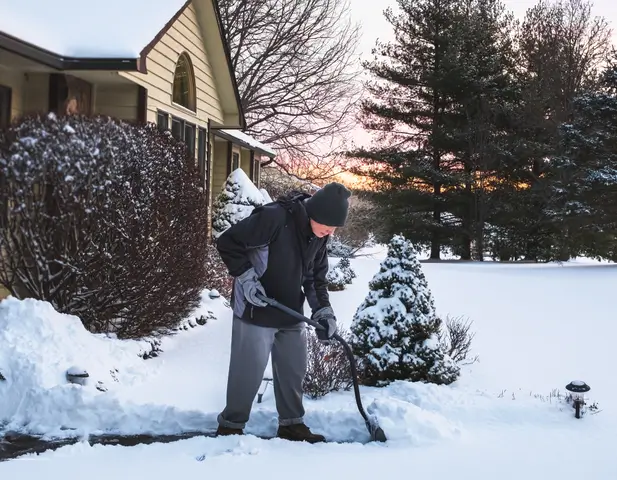 A homeowner shoveling the front sidewalk to their house.
