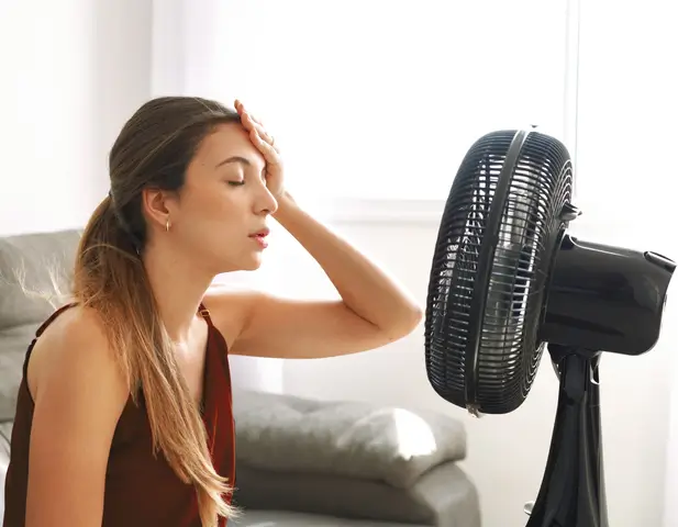 Woman standing in front of a floor fan, hot.