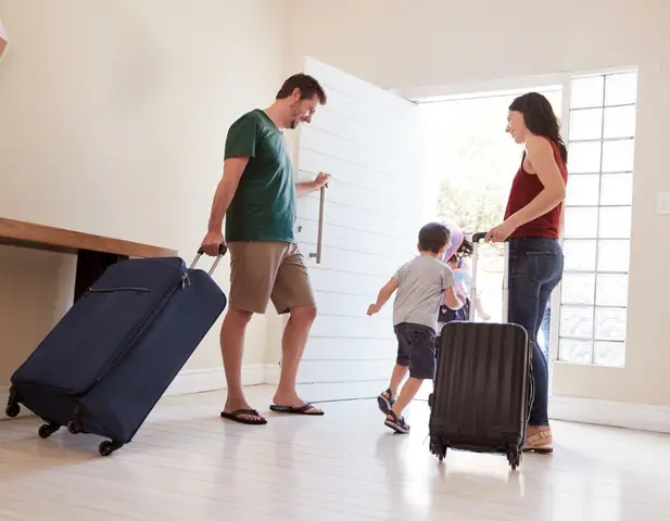 Family, with suitcases, headed out the front door of a beautiful home.