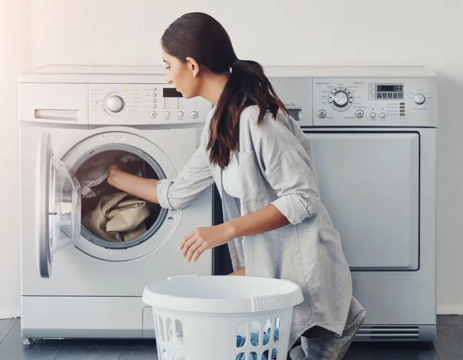A woman putting clothes into a washing machine.