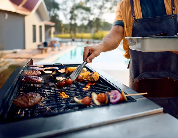 Man grilling burgers and vegetables on an outdoor grill.