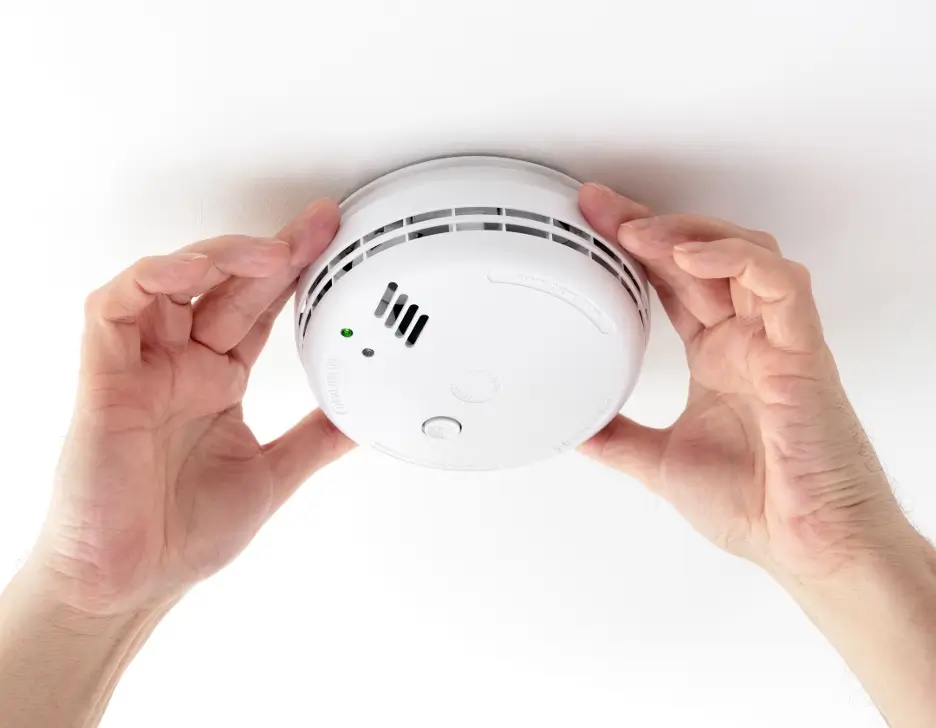 Hands replacing a smoke detector on the ceiling.