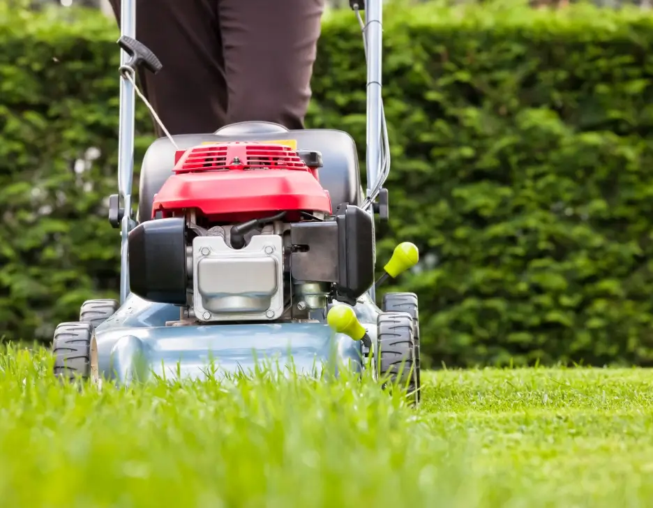 A person pushing a lawn mower over grass.