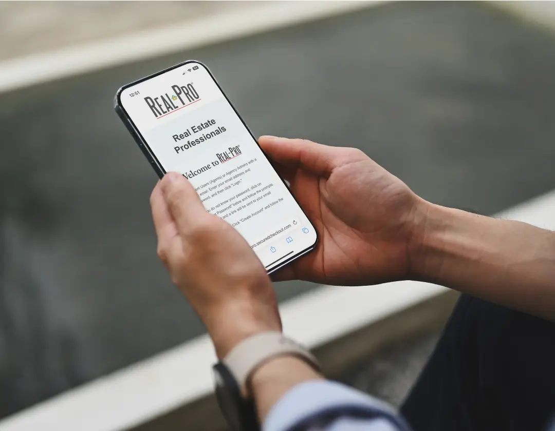 Hands holding a smartphone, with the Real-Pro homepage on display.