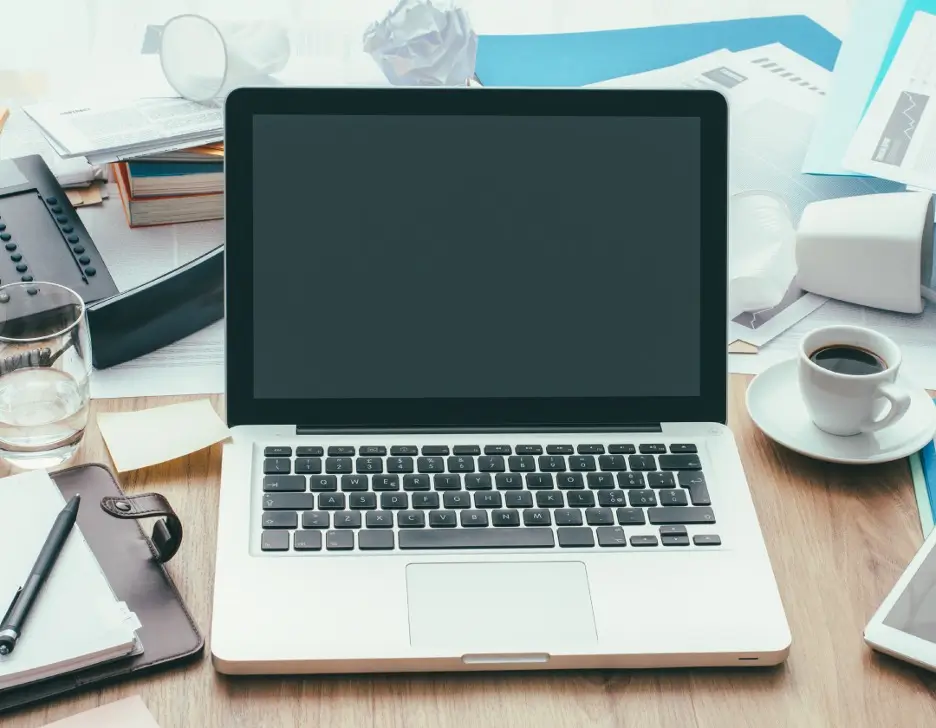 A cluttered office desk with an open laptop in the center.