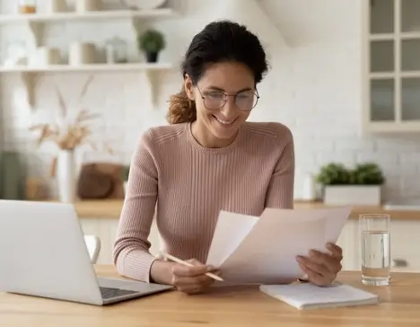 A woman sitting at a table, with her laptop and paperwork, reviewing her home warranty.