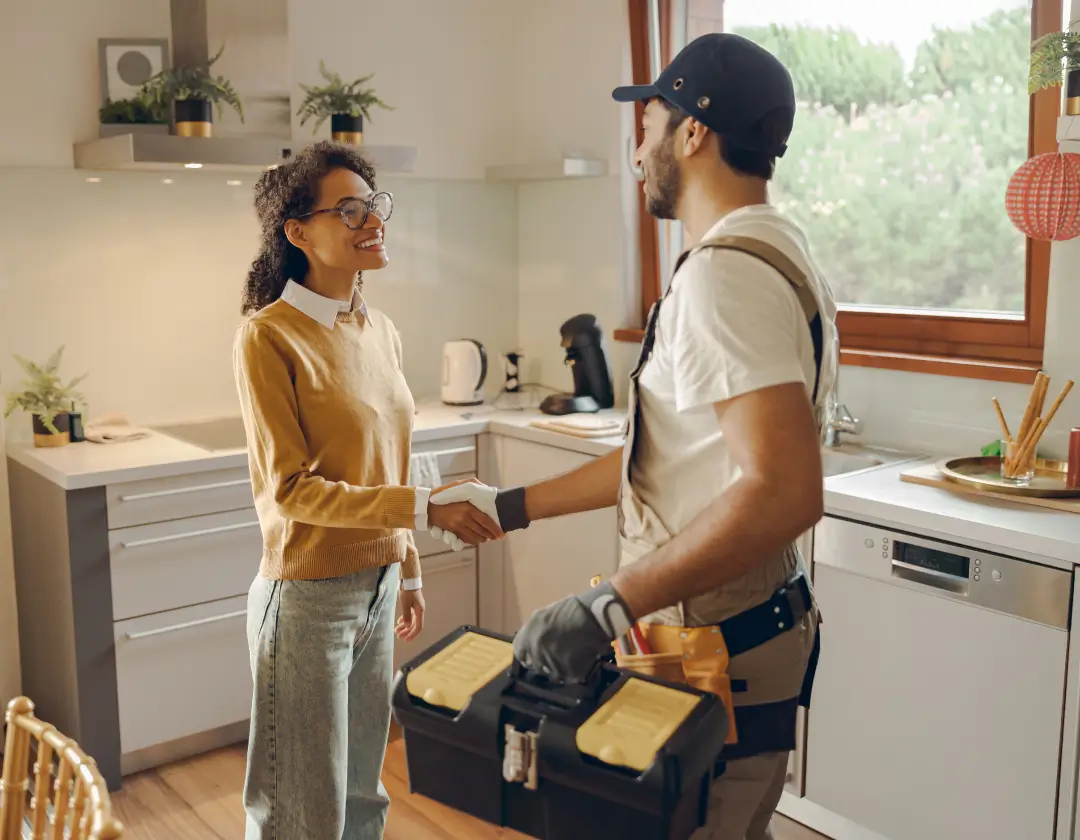 A homeowner shaking hands with a repair man inside her home.