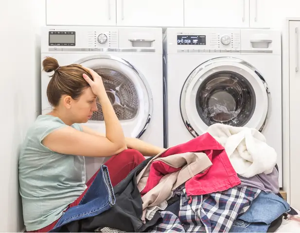 Woman sitting in front of her washer, with a pile of clothes, frustrated.