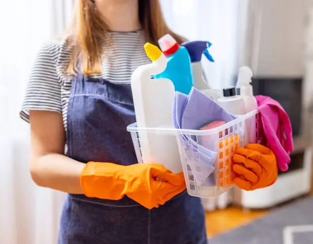 A woman standing with a bin of cleaning supplies.