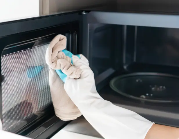 A person cleaning the outside of a built-in microwave.
