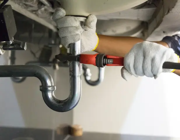 A maintenance worker repairing a pipe underneath a sink.