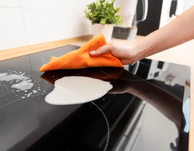 A homeowner cleaning up a spill on the stovetop that could be attractive to pests.
