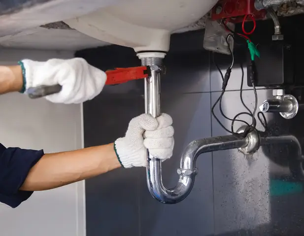 A contractor repairing the plumbing beneath a homeowner's sink.