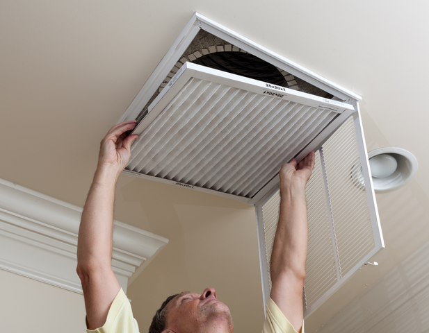 A man replacing an air filter inside his home, on the roof.