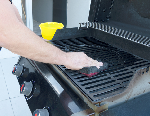 A man's hand using a brillo pad to clean the grill.