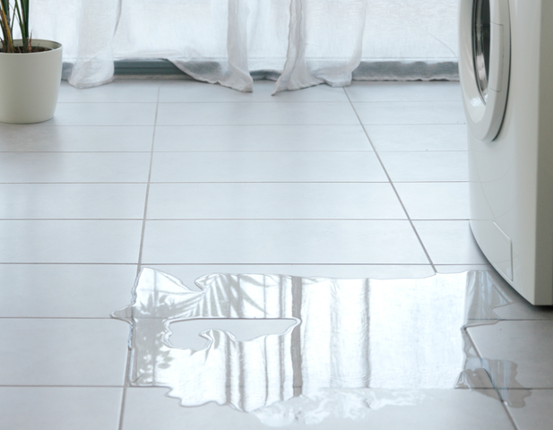 Water leaking out of a washing machine, onto the floor.