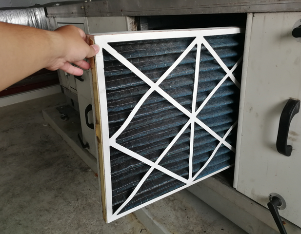 A hand holding out an air filter, showing how dirty it is.