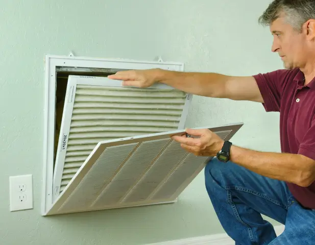 A homeowner changing his vent filters at home, striving to lower his energy bills throughout the season.